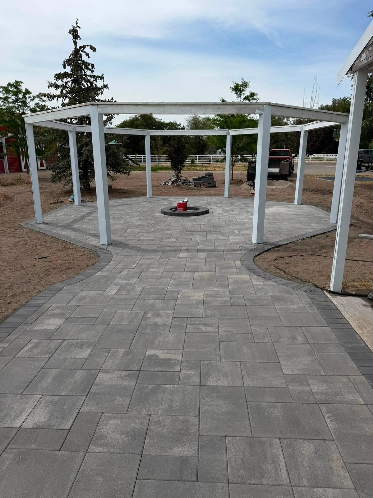 Grey paver patio and walkway under a white pergola with a centre firepit